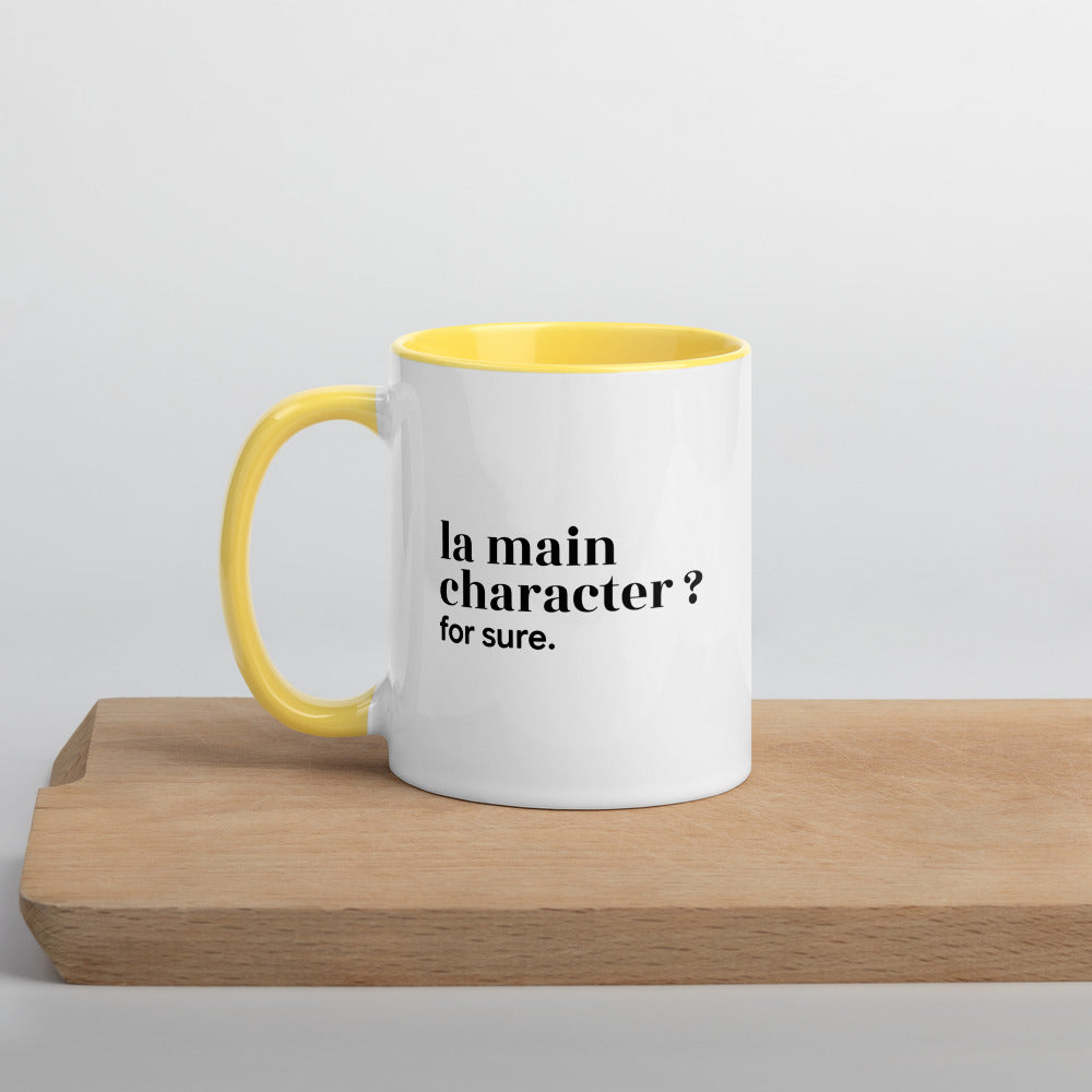 Mug intérieur jaune « la main character ? for sure. », sur une planche en bois