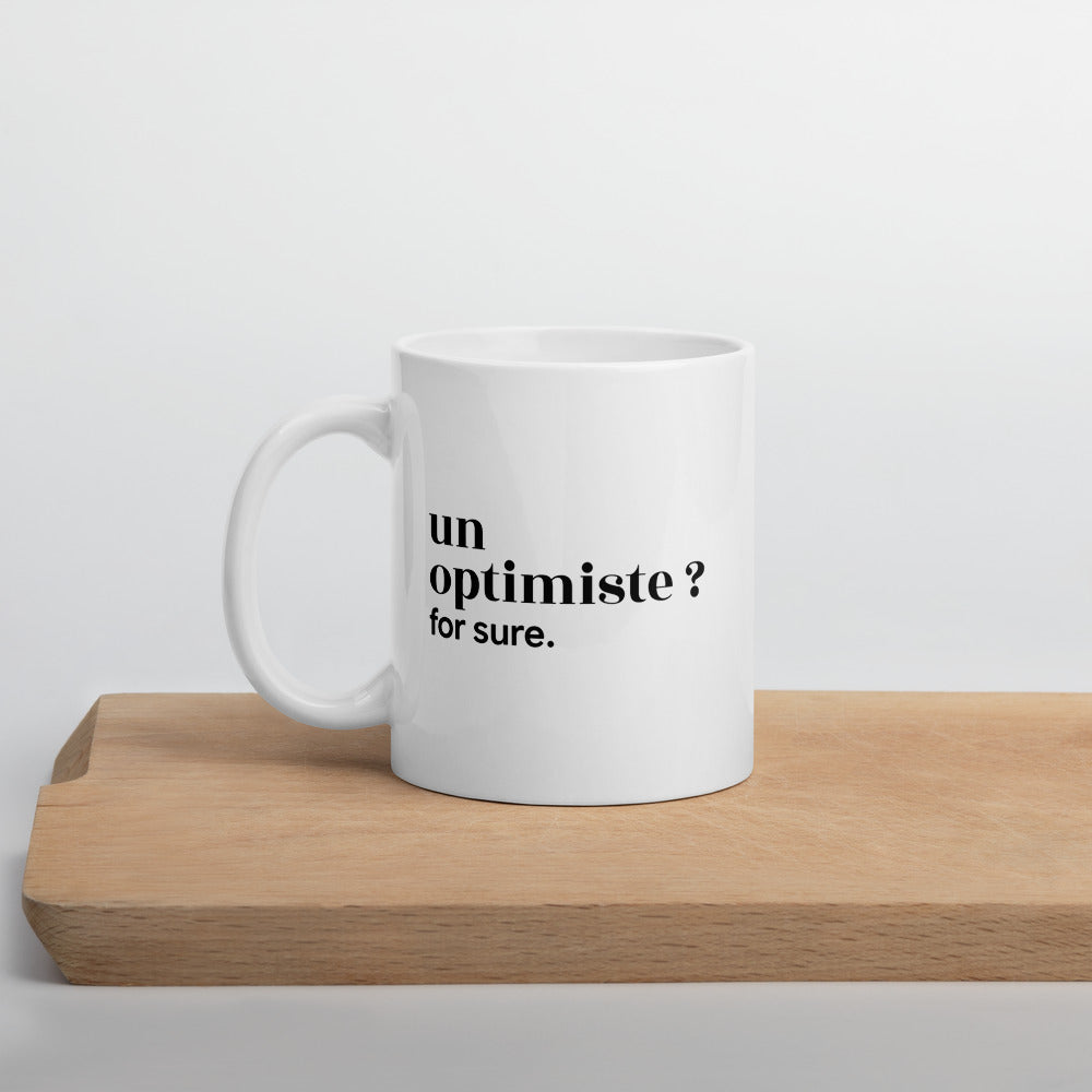 Mug blanc « un optimiste ? for sure. », sur une planche en bois